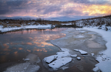 stream flowing through a snowy field at sunset