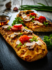 Focaccia - roasted mozzarella sandwiches with white mushrooms, tomatoes and prosciutto ham on black stone plate
