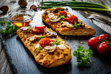 Focaccia - roasted mozzarella sandwiches with white mushrooms, tomatoes and prosciutto ham on black stone plate
