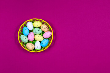 Obraz premium Multicolored Easter eggs in a bowl on a raspberry red background. Place for an inscription. View from above. Easter.