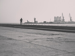 Moody scene with a lonely man walking on the seafront and the Mangalia shipyard in the background.