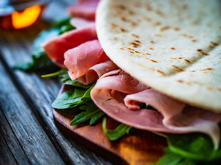 Italian piada wraps - piadina stuffed with fresh vegetable leaves and prosciutto ham on wooden table