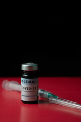 Covid-19 vaccine, red and black background, vaccine ampoule next to a syringe ready to vaccinate...