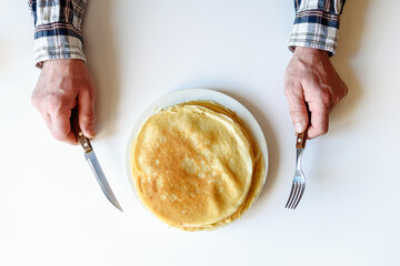Men's hands with a knife and fork. There are a lot of pancakes on a white plate.