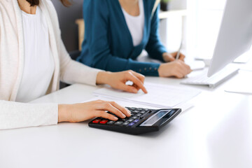 Accountant checking financial statement or counting by calculator income for tax form, hands close-up. Business woman sitting and working with colleague at the desk in office. Audit concept