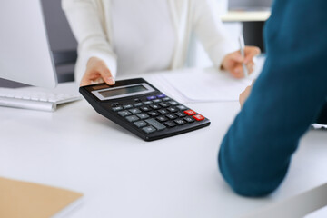 Accountant checking financial statement or counting by calculator income for tax form, hands close-up. Business woman sitting and working with colleague at the desk in office. Audit concept