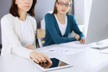 Businesswoman pointing at tablet computer screen while giving presentation to her female colleague. Group of business people working at the desk in office. Teamwork concept