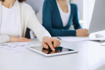 Businesswoman pointing at tablet computer screen while giving presentation to her female colleague. Group of business people working at the desk in office. Teamwork concept