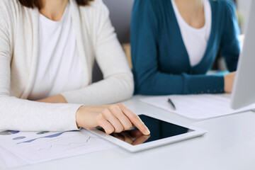 Businesswoman pointing at tablet computer screen while giving presentation to her female colleague. Group of business people working at the desk in office. Teamwork concept