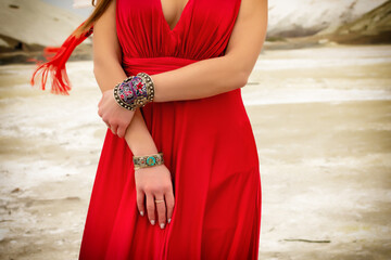 A woman in a red dress holds her hands in front. The woman is wearing beautiful bracelets.