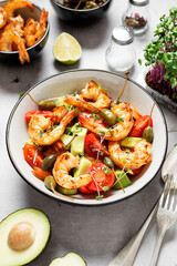 Easy grilled shrimp avocado salad with cherry tomatoes, capers and microgreens. Gray background.