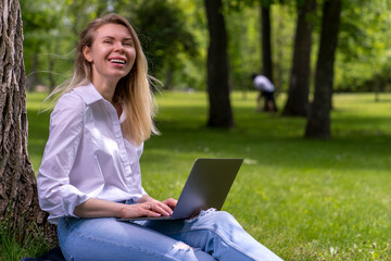 a girl with a smile communicates online using a laptop while sitting in a country park on a bench