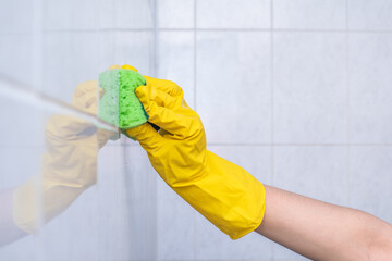 girl in yellow gloves washes the tiles in the bathroom. close-up.
