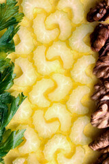 Sliced crescent-shaped celery bordered with walnut and parsley on a yellow background closeup