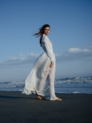 Fototapeta na wymiar Woman in white dress near the ocean barefoot portrait in full growth