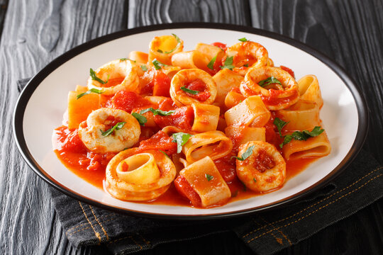 portion of Italian Calamarata pasta with squid rings and tomato close-up in a plate on the table. horizontal