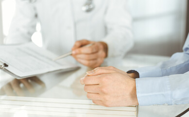 Fototapeta premium Unknown male doctor and woman-patient discussing current health examination while sitting in clinic and using clipboard. Good medical service in hospital. Medicine concept