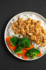 Homemade Orange Chicken with White Rice, Broccoli and Carrot on a plate on a black surface, top view. Flat lay, overhead, from above.
