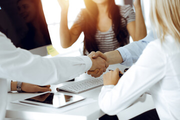 Two businessmen shaking hands in sunny office, close-up. Colleagues applauding of success meeting end