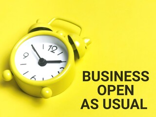 Business and time concept. Phrase BUSINESS OPEN AS USUAL written on yellow background with alarm clock.