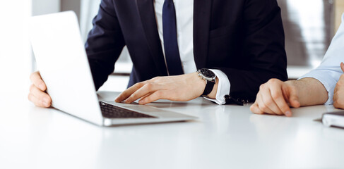 Obraz premium Unknown business people using laptop computer at the desk in modern office. Businessman or male entrepreneur is working with his colleague. Teamwork and partnership concept