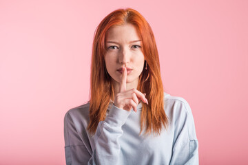 Redhead girl showing silence gesture in studio on pink background