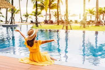 Young woman traveler relaxing and enjoying the sunset by a tropical resort pool while traveling for...