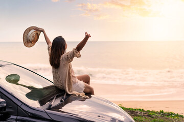 Young woman traveler sitting on a car and looking a beautiful sunset at the beach while travel driving road trip on vacation - obrazy, fototapety, plakaty