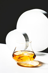 Contemporary still life with whiskey, scotch or bourbon in glass with shard ice on black white...