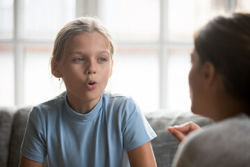 Small Caucasian teen girl child do articulation exercises with caring mother or teacher at home. Little kid pronounce sounds speak talk with tutor or coach, engaged in voice pronunciation together.
