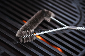 Cleaning outdoor gas grill with a metal brush before next grilling. Close-up.