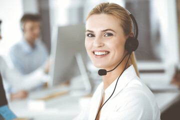 Blonde business woman using headset for communication and consulting people at customer service...