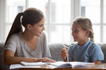 Smiling teen girl child and young mother sit at desk do homework chatting and talking. Happy Caucasian mom and small teenage daughter have fun preparing school home task together. Education concept.