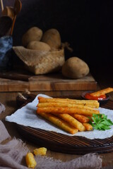 fried potato stick in a wooden board against dark background