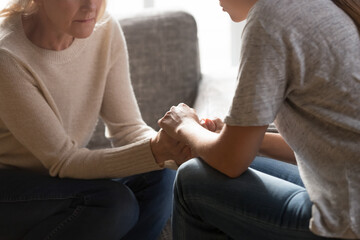 Crop close up of caring supportive adult daughter talk comfort unhappy lonely worried mature mother. Loving grownup female child hold hands caress upset depressed old mom feeling sad at home.