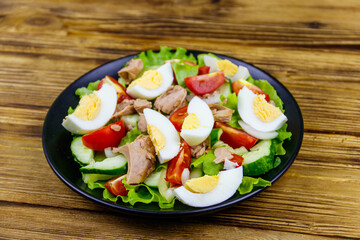 Tasty tuna salad with eggs, lettuce and fresh vegetables on wooden table