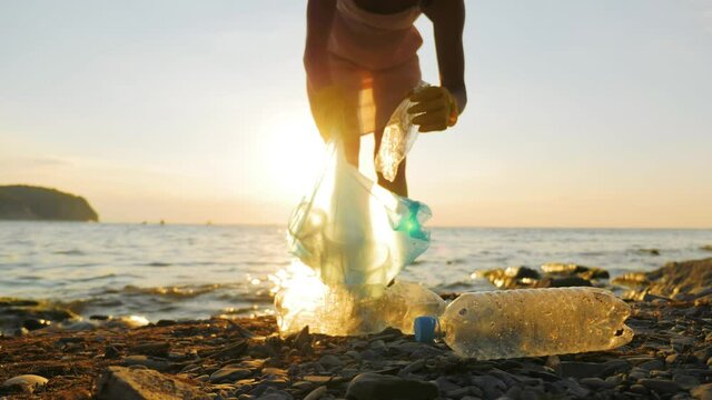 Hand woman in yellow gloves picking up empty plastic bottles cleaning on the beach. Volunteer picking up trash on the sea. Clean planet Earth, collect garbage, avoid pollution. Ecological problem.