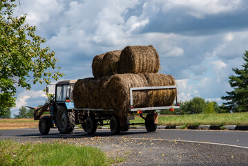 tractor driving on the road after collecting hay bales in summer under a stormy sky © Elizaveta Brunova