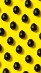 Easter pattern made with black painted eggs on vibrant yellow background. Minimal food concept. Flat lay.