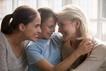 Obraz na płótnie Canvas Overjoyed three generations of Caucasian women relax together cuddle in cozy home at family weekend. Happy little girl child with young mother and older grandmother rest showing unity and bonding.