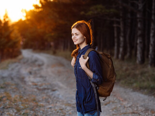 Woman on the road with a sunset sun backpack and forest in the background