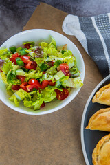 Fresh small salad side dish served with a plate of Empanadas - traditional Latin American baked beef pastry placed in a plate. Salas contain lettuce, cherry tomatoes, green onion, and cucumber.