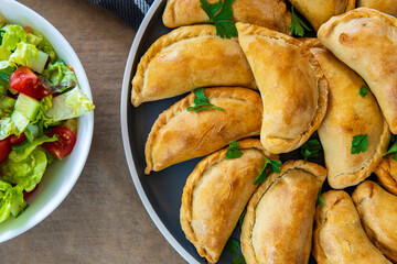 Traditional Latin American baked beef empanadas on a plate with a fresh salad sidedish. Gluten free savory pastries with meat stuffing or filling. Handmade typical dish in Spain or Argentina. Close up