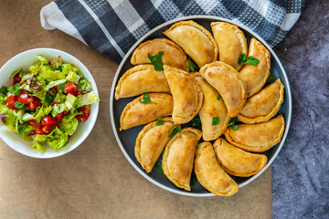 Traditional Latin American baked beef empanadas on a plate with a fresh salad sidedish. Gluten free savory pastries with meat stuffing or filling. Handmade typical dish in Spain or Argentina. Top view