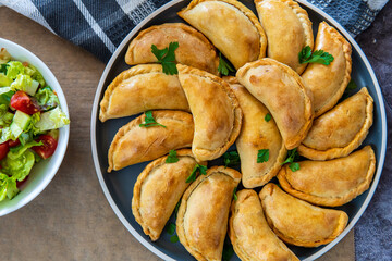 Empanadas - traditional Latin American baked beef pastry on a plate with a fresh salad sidedish. Gluten free savory appetizer with meat stuffing or filling. Handmade typical dish in Spain or Argentina