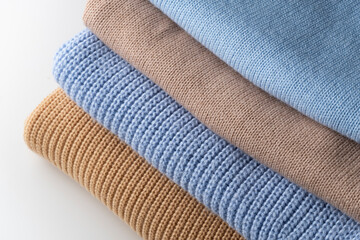 A stack of 4 wool sweaters in beige and blue colors.