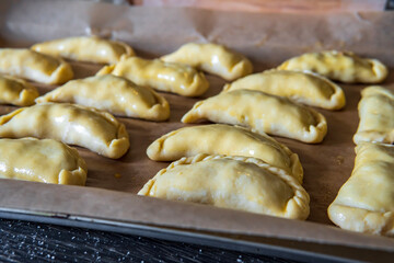 Uncooked empanadas on a baking tray. Traditional Latin American baked beef pastry ready for the oven. Gluten free savory appetizer with meat filling. Handmade typical dish in Spain or Argentina. Side 