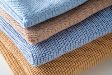 A stack of 4 wool sweaters in beige and blue colors.
