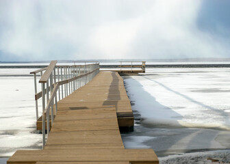 Obraz premium winter landscape on a wooden footbridge in the lake, the surface of the lake is partially covered by ice, cold winter day by the lake, Lake Burtnieki