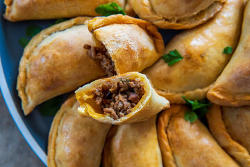 Empanadas - traditional Latin American baked beef pastry on a plate cut into half. Gluten free savory appetizer with meat filling or stuffing. Handmade typical dish in Spain or Argentina. Close up.